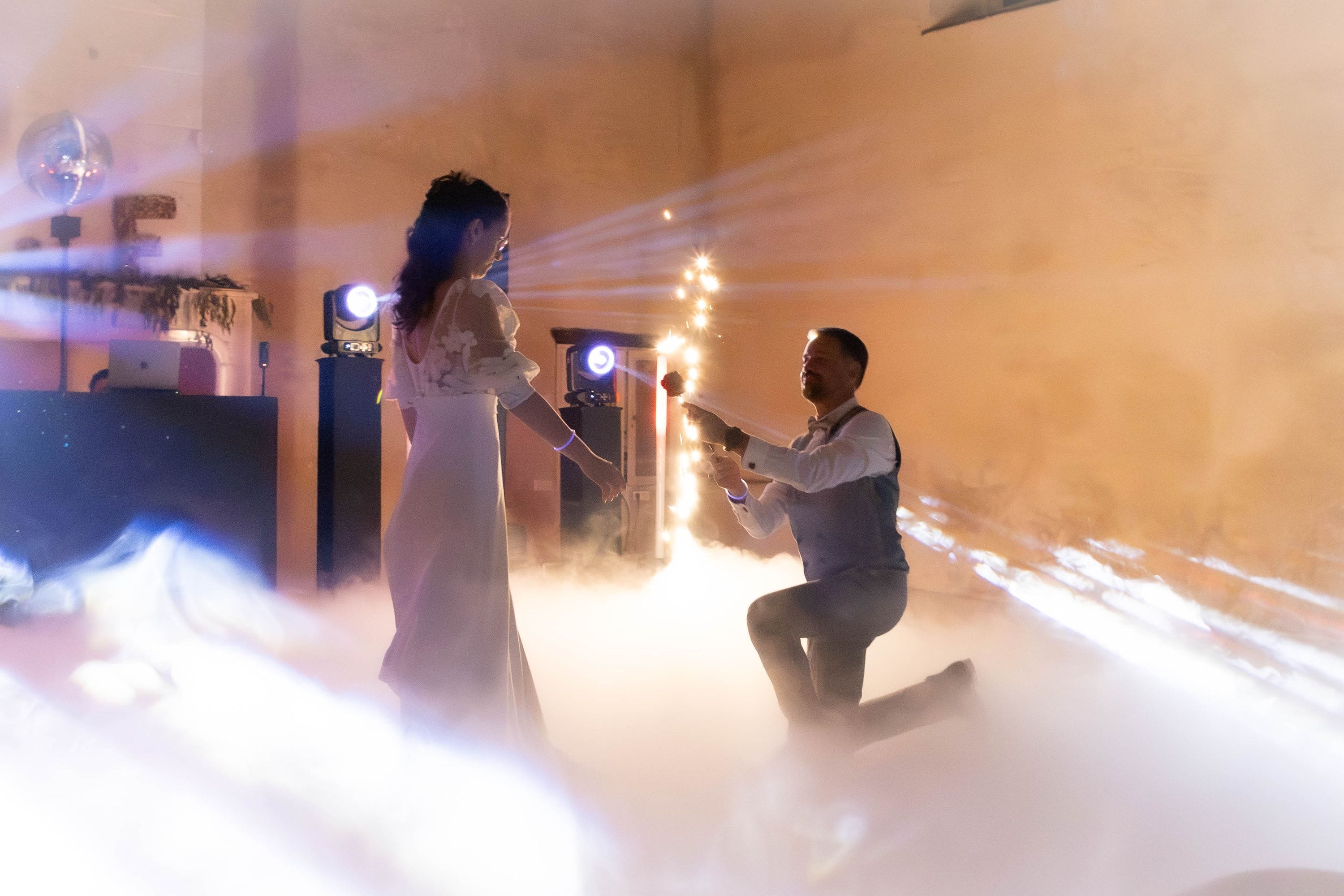 Le marié à genoux devant la mariée, dans la fumée lourde et les faisceaux lumineux