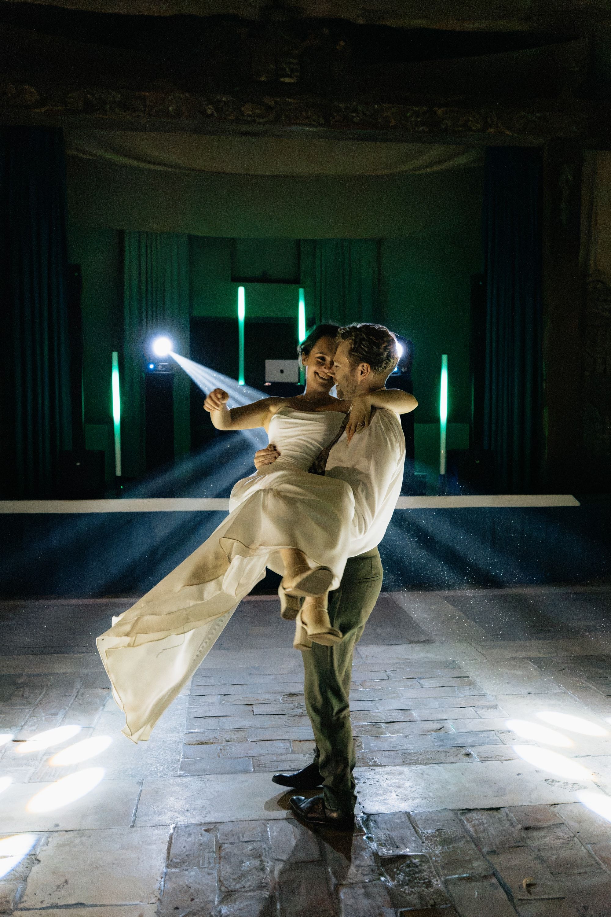 Le marié soulève la mariée pendant l’ouverture de bal, sous les faisceaux lumineux