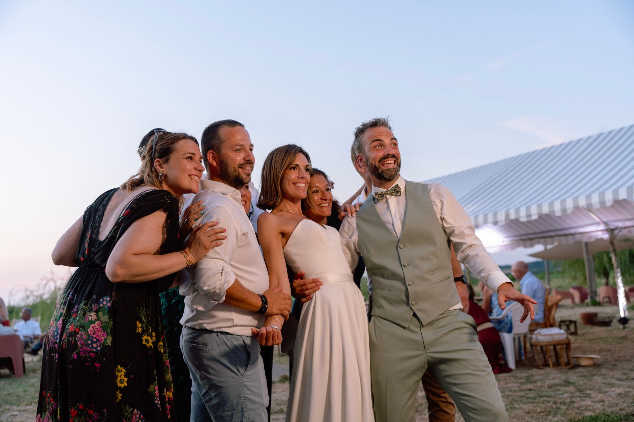La mariée et ses invités posent devant le photobooth, en plein air au coucher du soleil